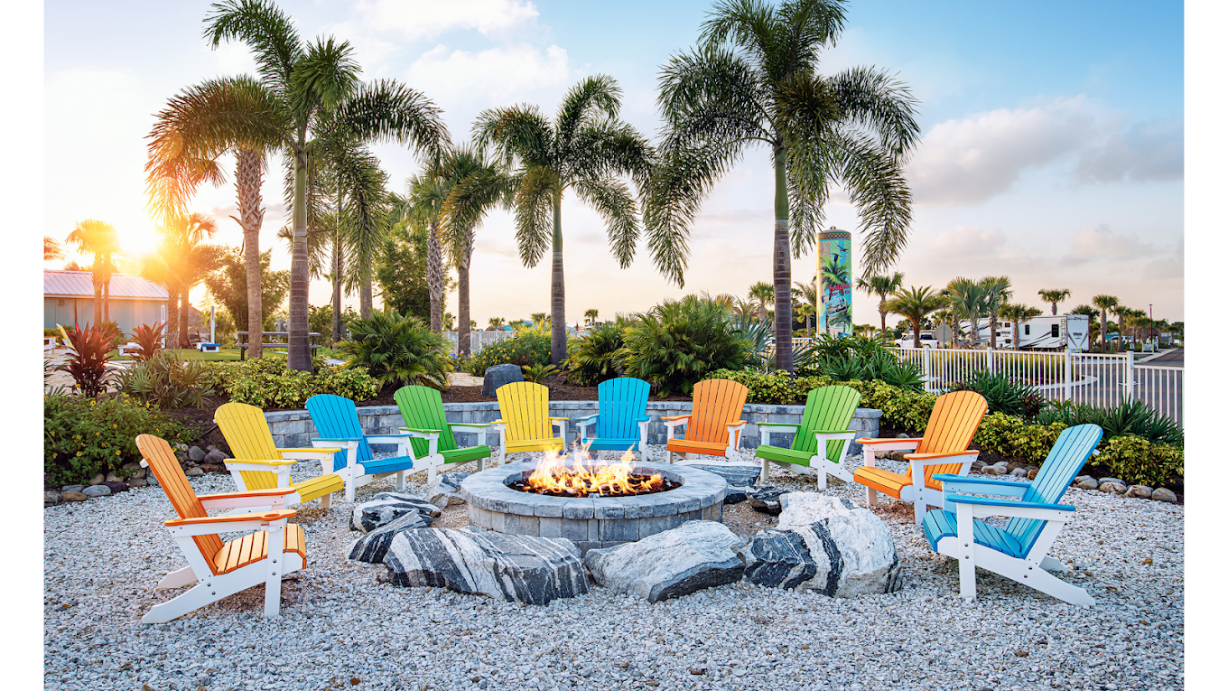 Sunset fire pit ringed by colorful Adirondack chairs beneath palm trees at Camp Margaritaville