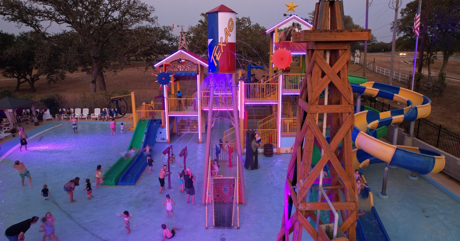 Dusk aerial view of the Texas-themed water play zone, slides and splash pool at Texas Wine Country Camp-Resort in Fredericksburg, Texas