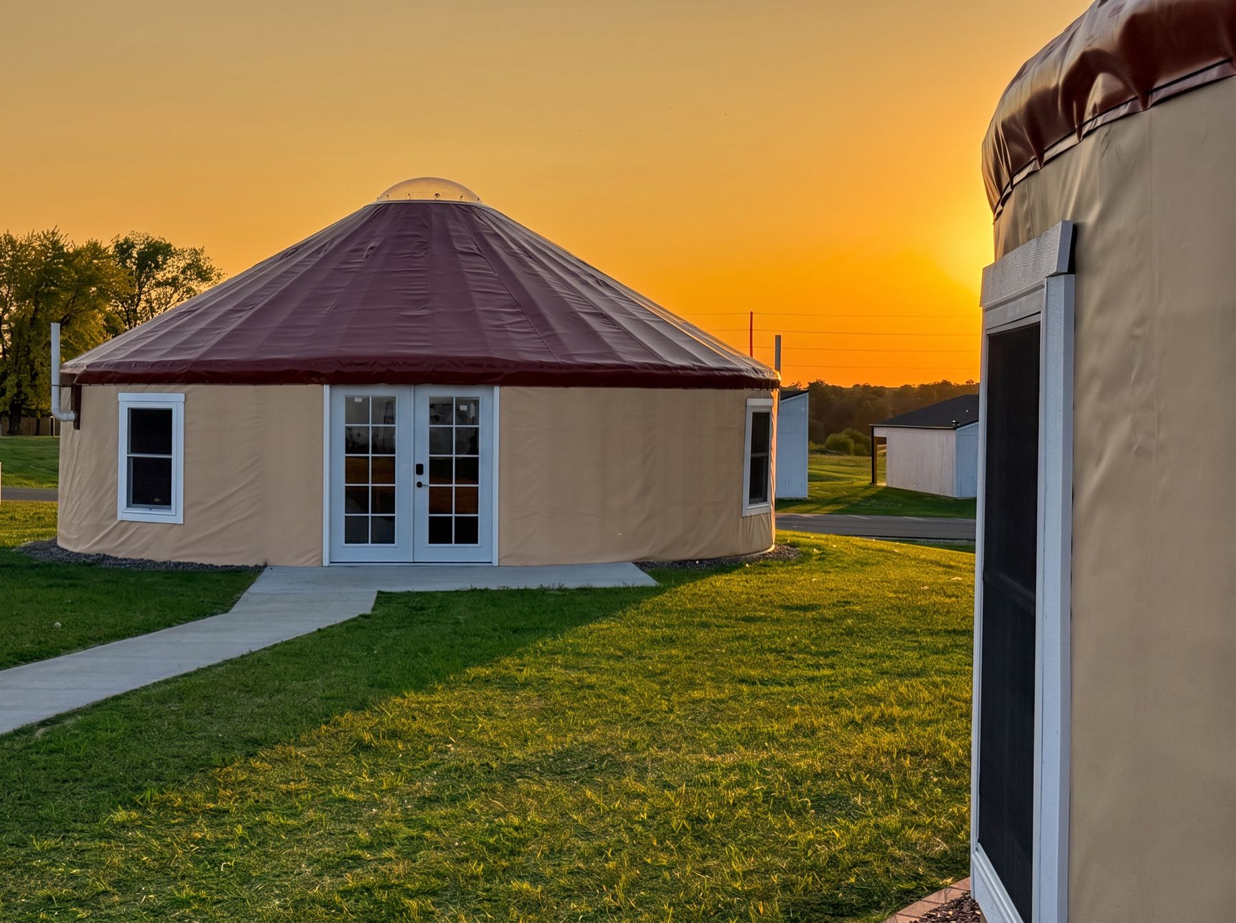 Canvas yurt lodging unit with french doors and mowed lawn at golden-hour sunset